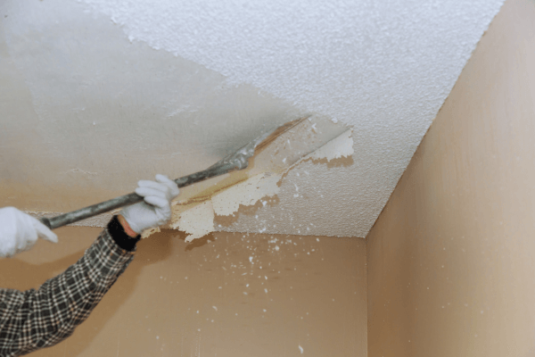 man scraping off popcorn ceiling in home